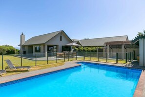 A modern house with a swimming pool, a covered patio, and a fenced backyard.