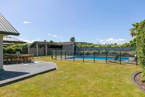 A backyard with a swimming pool, a covered patio, and a seating area. - Watene Lodge - Spacious 5 Star Home with Pool (Taupo)