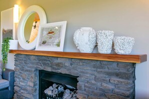 A fireplace with a stone mantle, a framed picture, and three textured vases on the mantel.