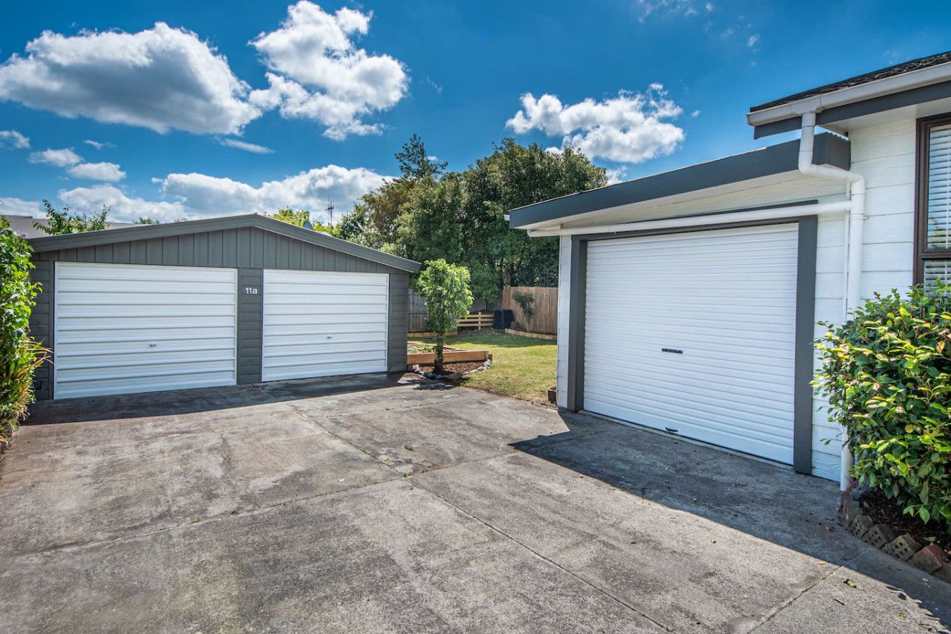 A residential garage with a concrete driveway and a small tree in the center.