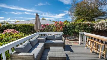 Une terrasse extérieure couverte, aménagée avec un canapé en osier, un banc et une pergola dotée d’un auvent.
