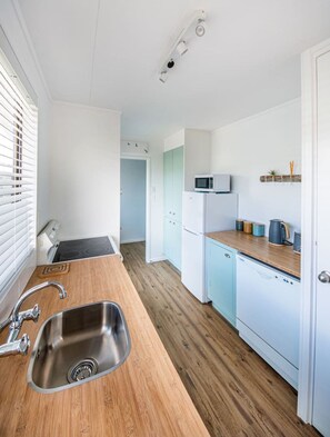 Une cuisine moderne dotée d’un évier en acier inoxydable, d’un plan de travail en bois, de meubles blancs et d’un four à micro-ondes.