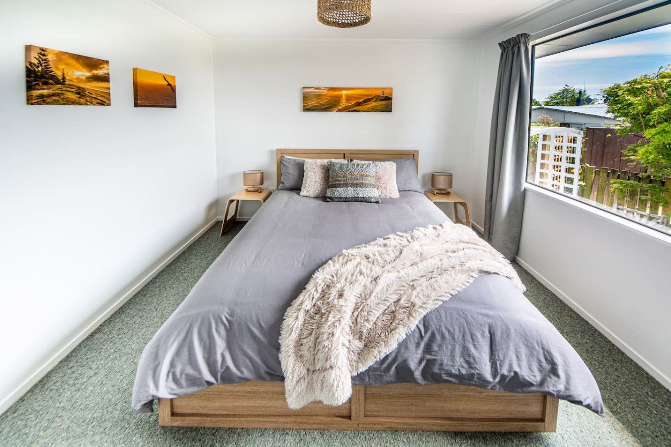 A bedroom with a bed, two bedside tables, and three wall-mounted paintings.