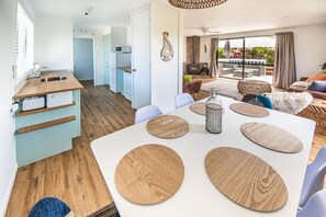 Ein modernes Wohnzimmer mit weißem Esstisch, Holzakzenten und Blick ins Freie.