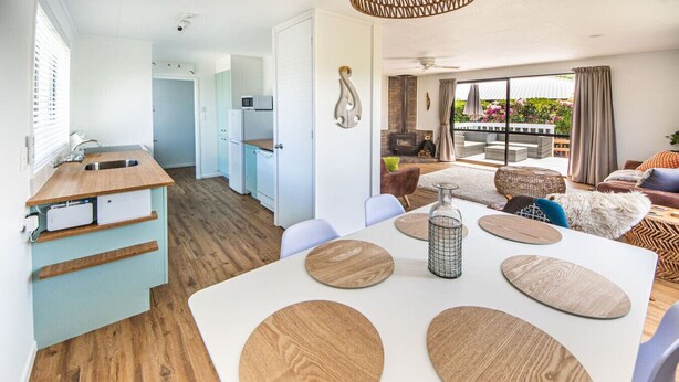 Una sala de estar moderna con una mesa de comedor blanca, detalles de madera y vistas al exterior.