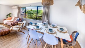 Un comedor moderno con una mesa blanca dispuesta para seis personas, rodeada de sillas blancas con patas de madera.