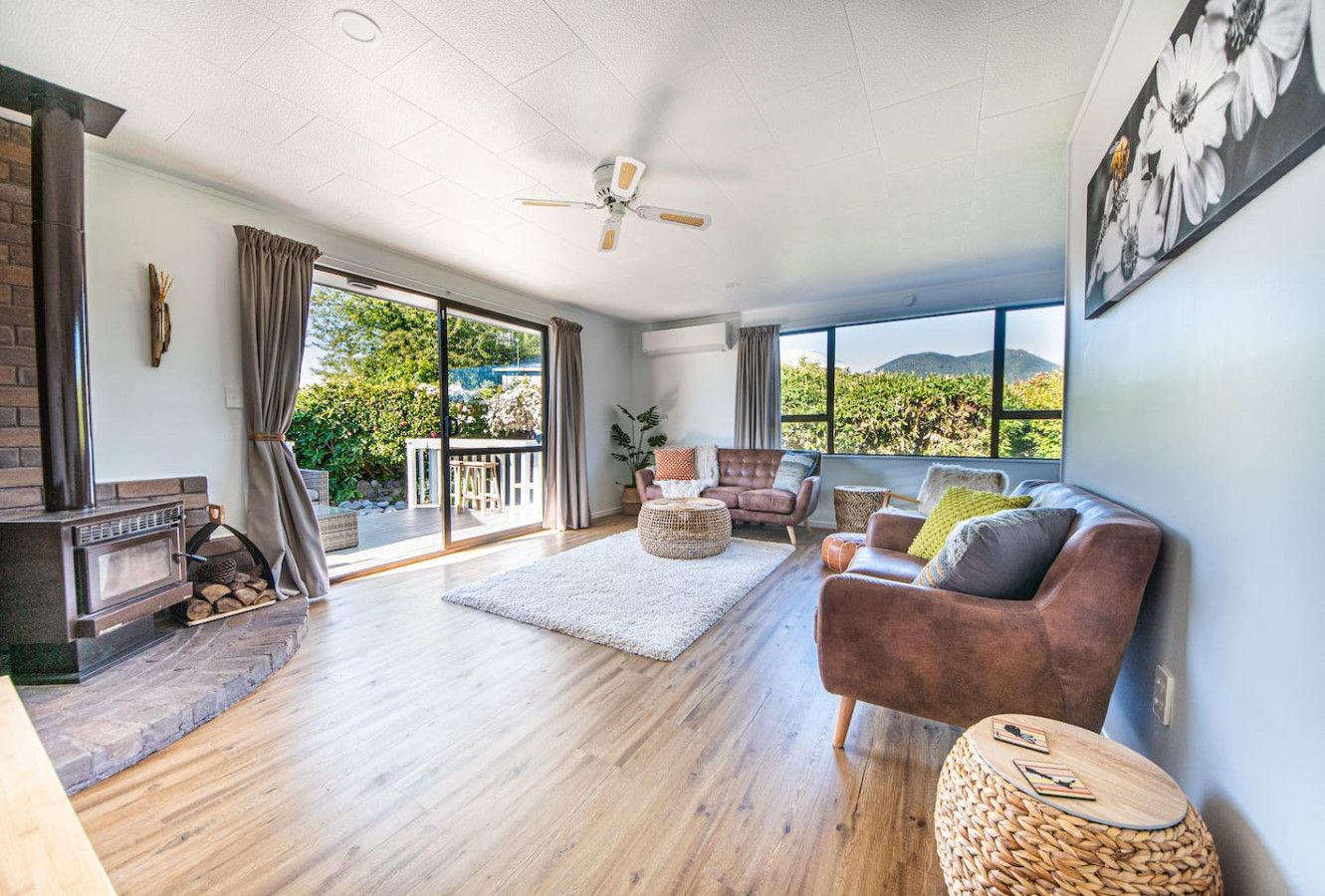 A spacious living room with a fireplace, a ceiling fan, and a large window offering a view of greenery.