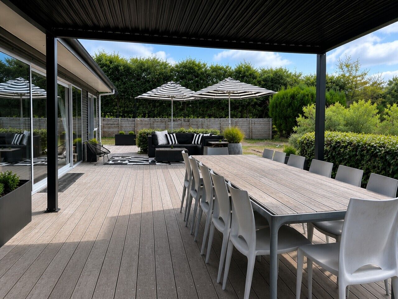 An outdoor patio with a wooden deck, a long table with chairs, and a sofa set.