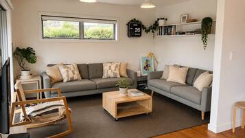 A living room with a grey sofa, a wooden coffee table, a rocking chair, and a bookshelf with plants.