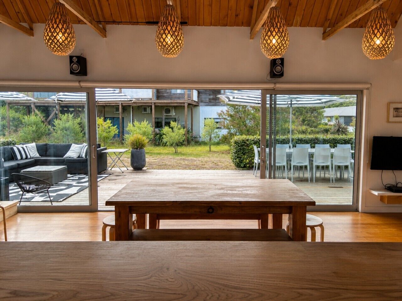 A spacious room with a wooden table and benches, large windows, and a view of an outdoor patio area.
