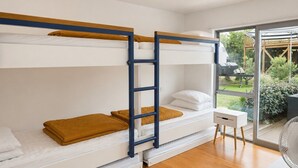 A bunk bed room with a wooden floor, a small white bedside table, and a window with a view of a garden.
