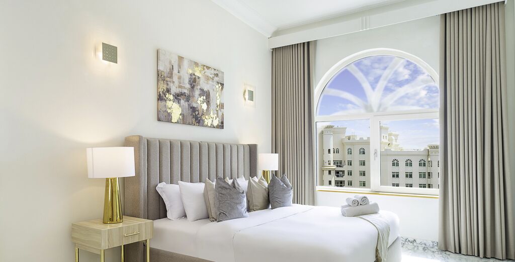 Camera d'albergo con un letto grande, un comodino con una lampada, un quadro appeso al muro e vista sugli edifici attraverso una finestra.