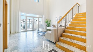 Amplia sala de estar con techo alto, un ventanal grande y una escalera con peldaños amarillos.