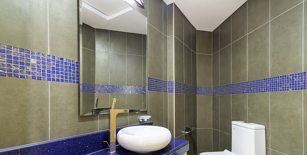Un baño con tocador azulado, un lavabo blanco y un espejo encima.