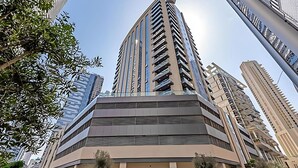 A modern multi-story building with a prominent corner entrance, large windows, and a flat roof. - Livbnb-2B+Maid's in Dunya, 5Min Walk to Dubai Mall (Dubai)