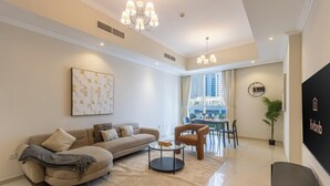 A modern living room with a sofa, coffee table, and a dining area with chairs and a table. - Livbnb-2B+Maid's in Dunya, 5Min Walk to Dubai Mall (Dubai)
