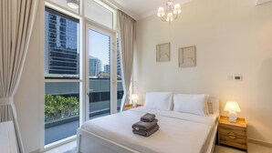 A hotel room with a large bed, two bedside tables, a chandelier, and a view of the city through large windows. - Livbnb-2B+Maid's in Dunya, 5Min Walk to Dubai Mall (Dubai)