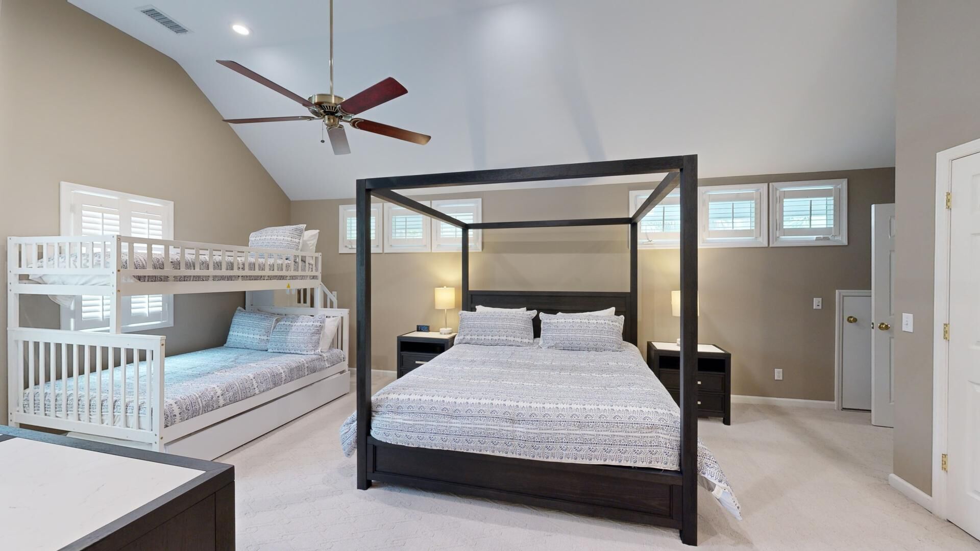 Un dormitorio con cama con dosel, ventilador de techo, literas y un ventanal grande.