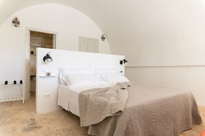Quarto com cama, mesa de cabeceira, luminária na parede e porta para o banheiro.