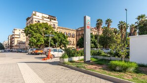 Une zone piétonne dallée, avec un cheminement tactile pour les personnes malvoyantes, un panneau de signalisation et des voitures garées.