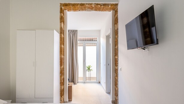 Une chambre d’hôtel avec un lit, une armoire, une télévision et une vue sur un balcon verdoyant, accessible par une porte.