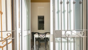 Une pièce avec une table blanche et deux chaises, une petite fenêtre et une porte avec des barreaux en métal.