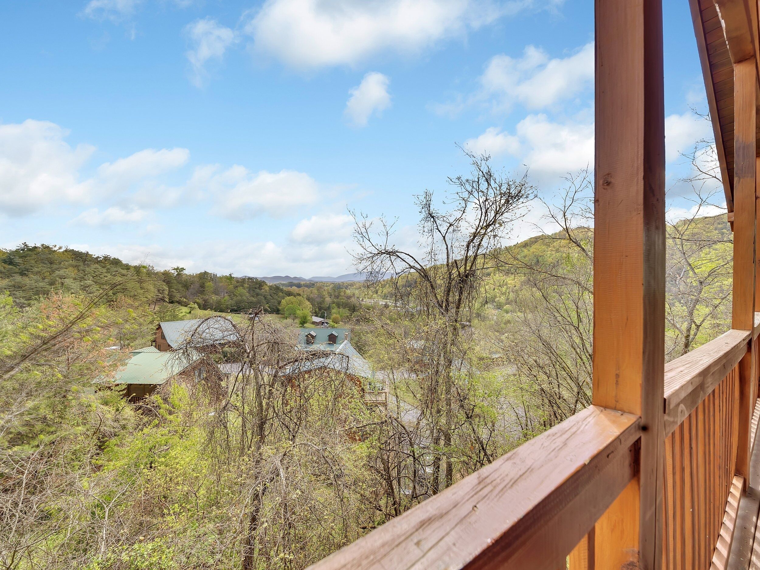 Une vue depuis un balcon en bois donnant sur une zone boisée, avec une maison visible au loin.