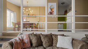 Una sala de estar con un sofá de cuero marrón, un comedor con sillas de madera y una mesa, y una cocina con armarios verdes.