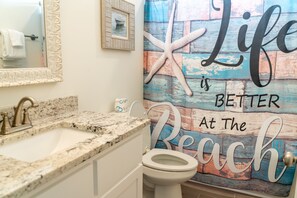 A bathroom with a granite countertop sink, a white toilet, and a wall with a painted message. - Sunset Blessing - 207 Arias Ct 4 Bedroom Home (Dauphin Island)