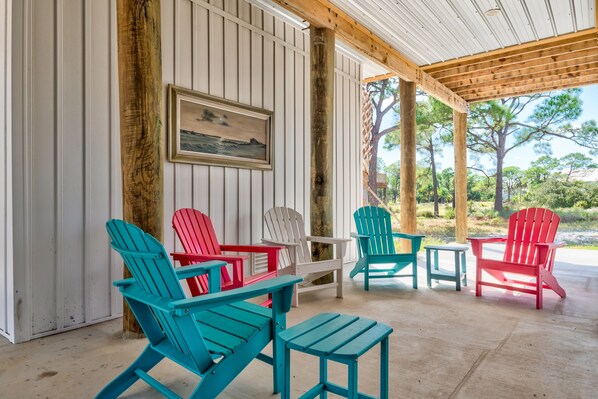 Un espace extérieur abrité, aménagé avec des chaises Adirondack rouges, blanches et turquoise, une table en bois et un banc.