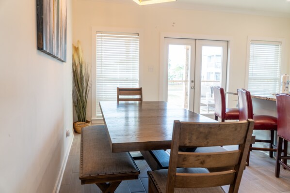 Un comedor con una mesa y sillas de madera, una planta en maceta y vistas por la puerta.