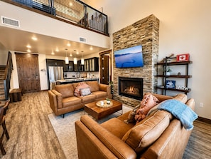 A spacious living area with a fireplace, a kitchen in the background, and a staircase leading to an upper level. - Silverado Sanctuary 2 Bedroom Condo (Park City)