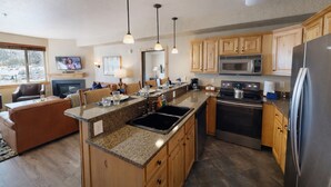 A modern kitchen with granite countertops, wooden cabinets, stainless steel appliances, and pendant lighting.