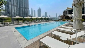 A rooftop pool with lounge chairs and umbrellas, surrounded by high-rise buildings.