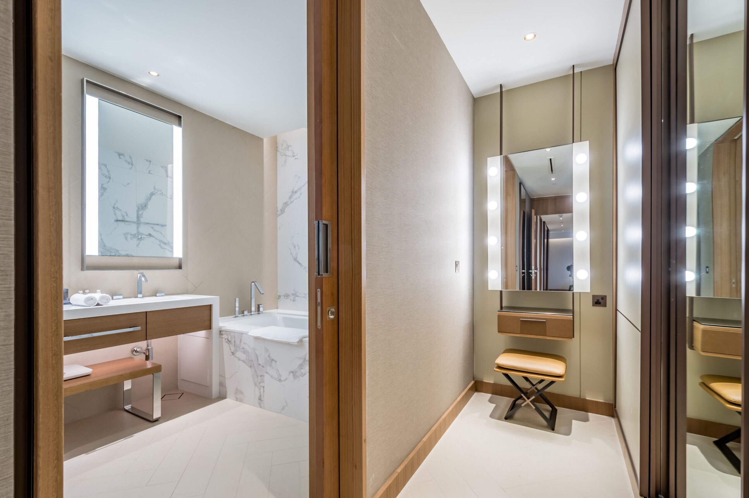 A modern bathroom with a marble sink, vanity, and a bench.