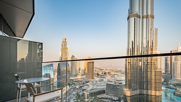 A modern hotel room with a balcony overlooking a cityscape, featuring a large window and a seating area.