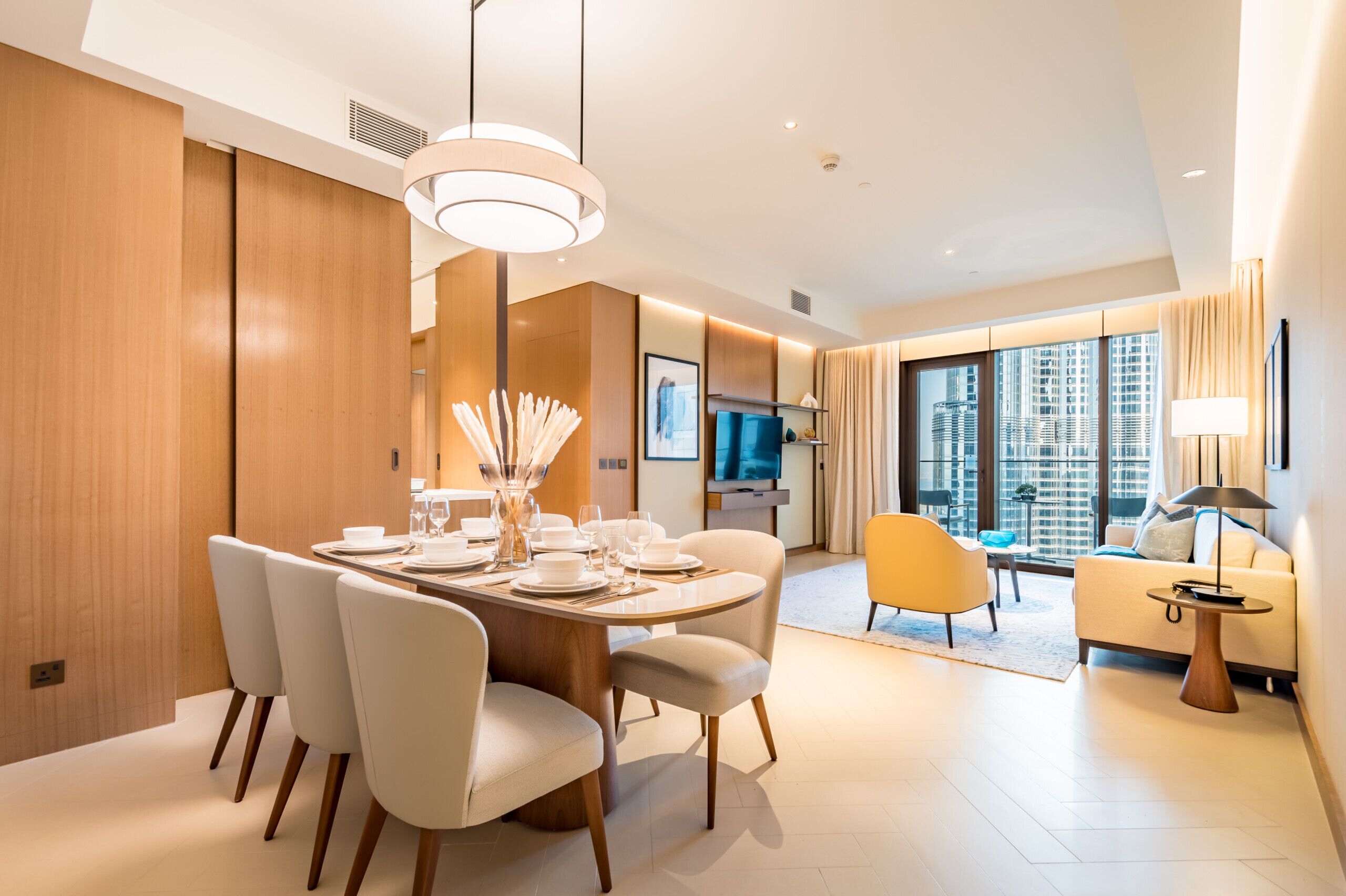 A modern hotel room with a dining area, a sofa, and a TV.
