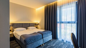 Une chambre d’hôtel avec un lit double, une table de chevet, une chaise et une grande fenêtre avec des rideaux.