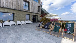 Un espace extérieur aménagé avec des chaises en plastique blanc et un bâtiment en bois doté de grandes fenêtres.