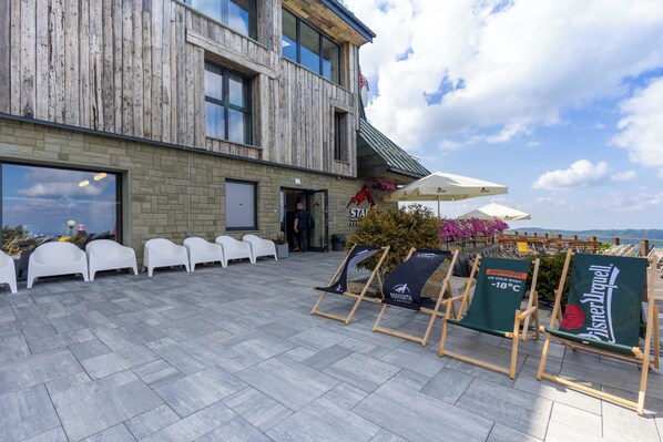 An outdoor seating area with white plastic chairs and a wooden building with large windows. - Start Skrzyczne (Szczyrk)