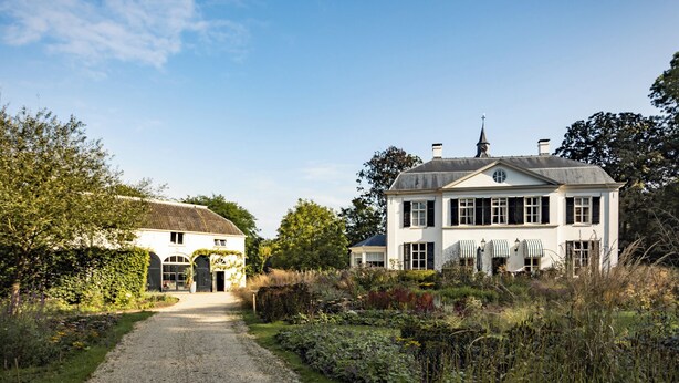 A two-story white house with a gravel driveway leading to a gated entrance.