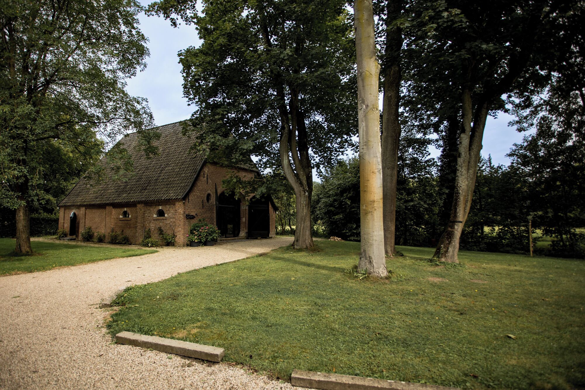 A rustic brick building with a thatched roof, surrounded by a well-maintained lawn and tall trees.