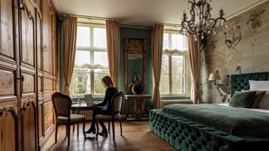 A room with a large bed, wooden wardrobe, a desk with a chair, and a window with curtains.