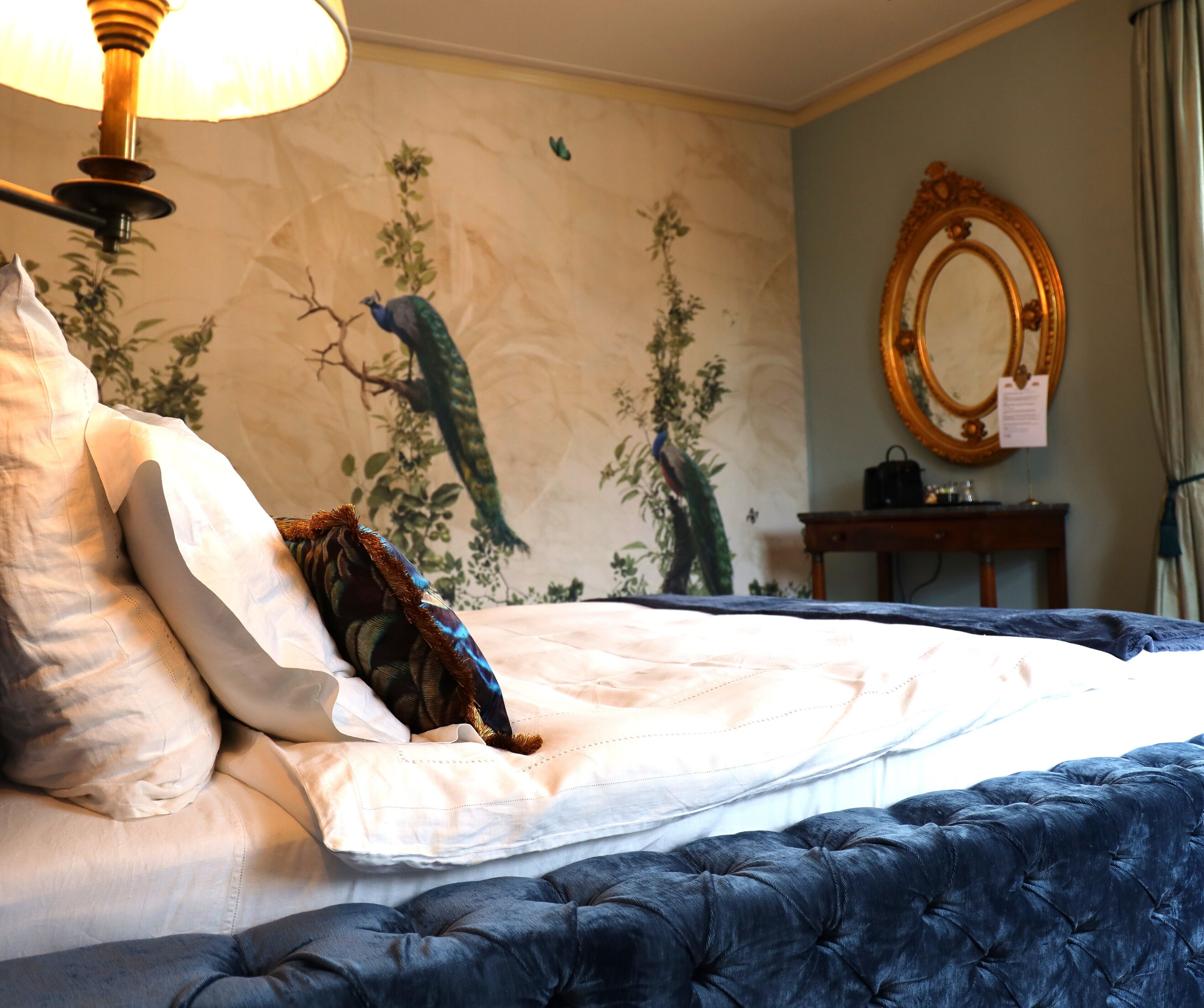 A hotel room with a bed, a wall mural, a mirror, and a nightstand.