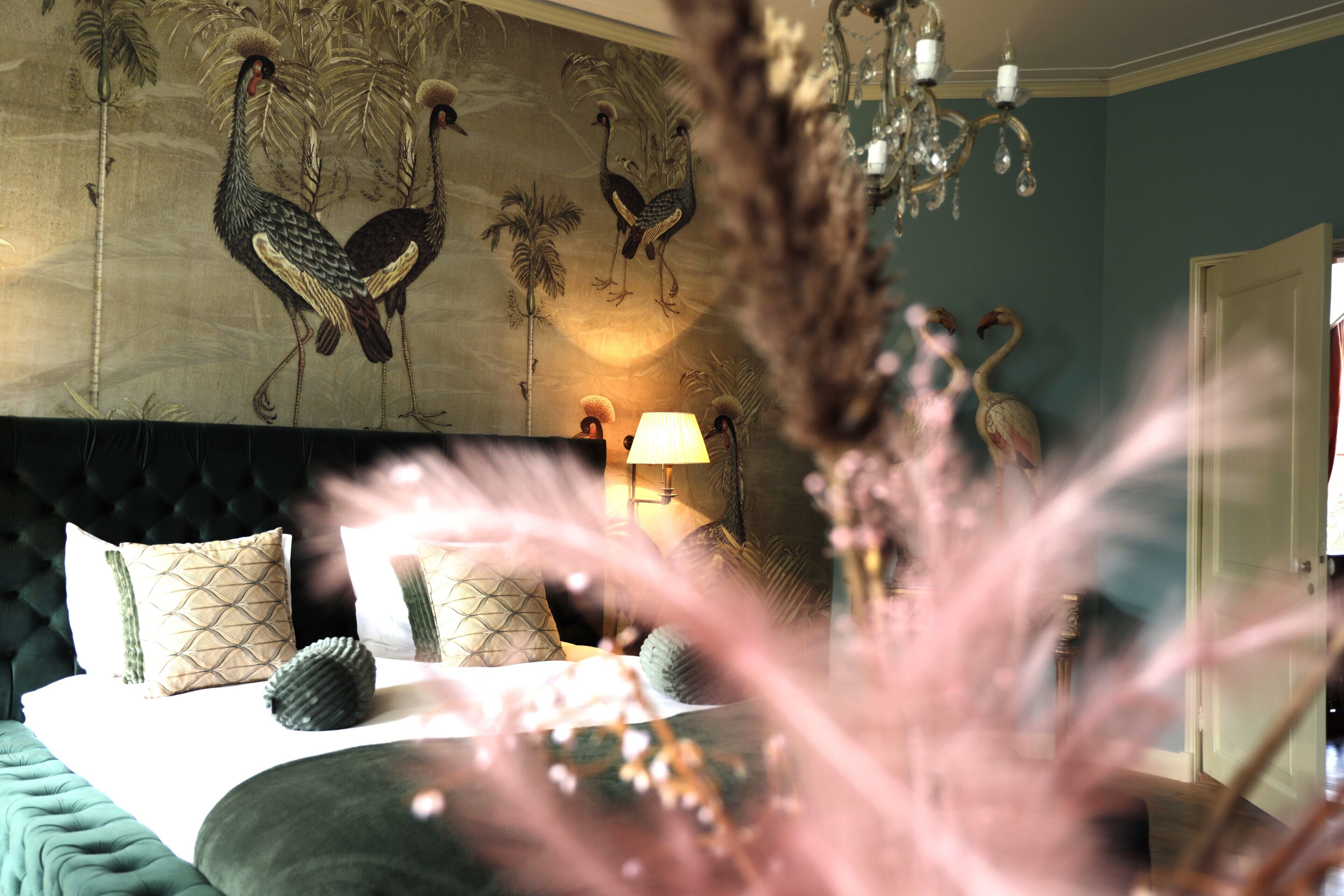 Une chambre avec un grand lit, un lustre et une fresque murale représentant des oiseaux.