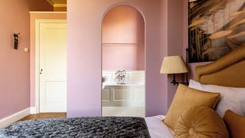 Une chambre à coucher avec un lit, une table de chevet, une lampe et une vue sur la salle de bain à travers une arche.