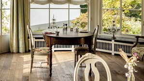 A dining area with a wooden table, white chairs, and a view of greenery outside.