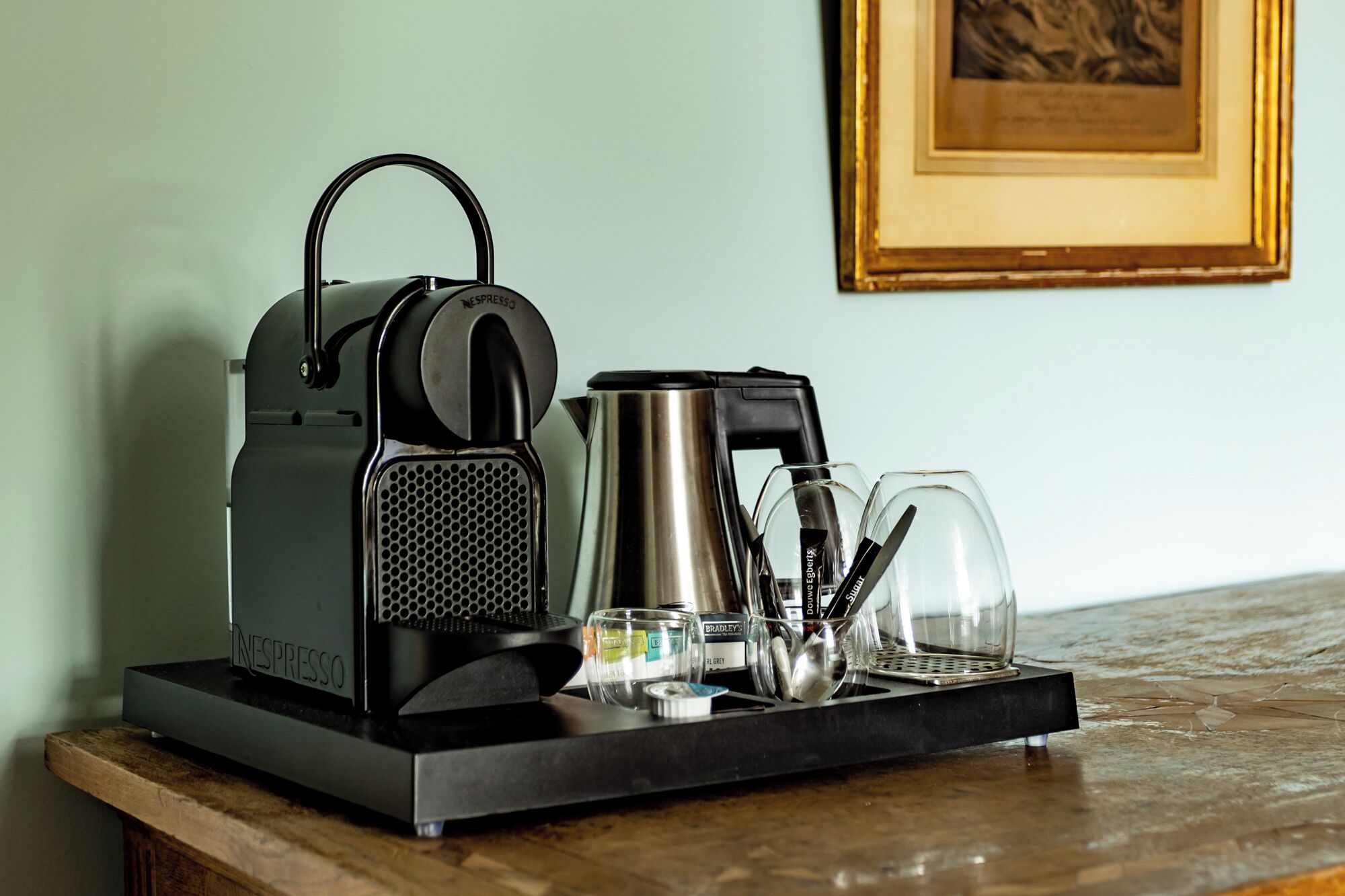 A coffee machine, a kettle, and a tray with glasses and utensils on a table.