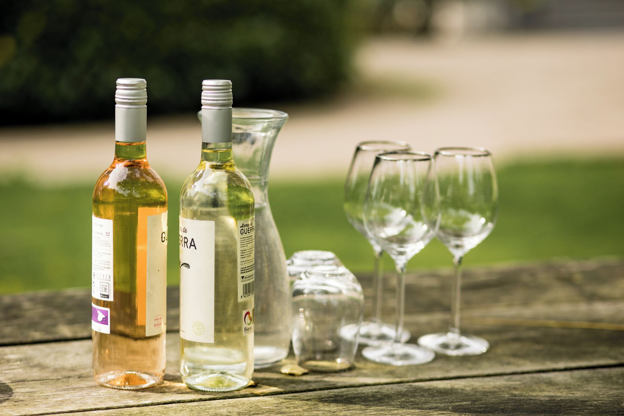 Three bottles of wine and four empty wine glasses on a wooden table.