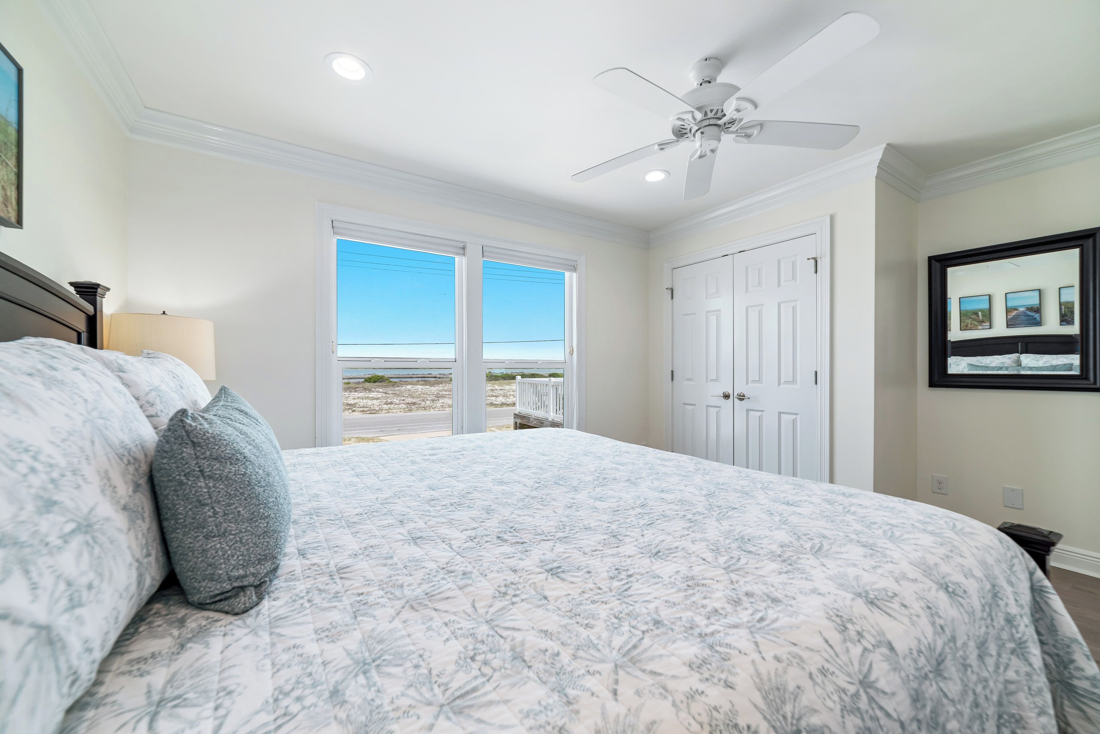 Une chambre avec un grand lit, un ventilateur de plafond et une vue sur la plage, accessible par une porte coulissante.
